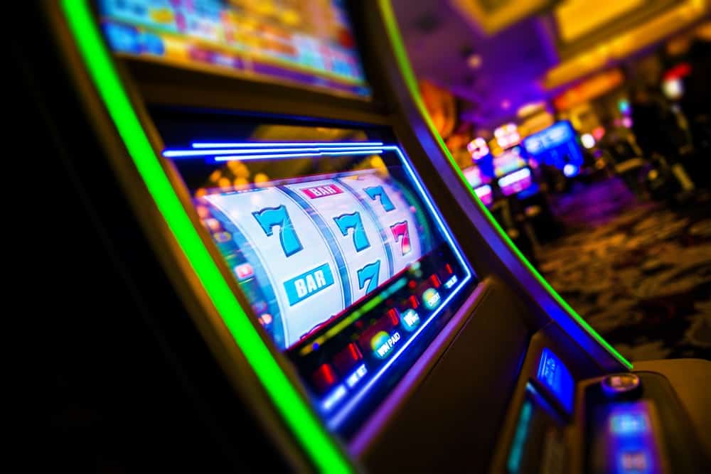 Spielautomat bzw. Einarmiger Bandit im Vordergrund innerhalb eines Casinos